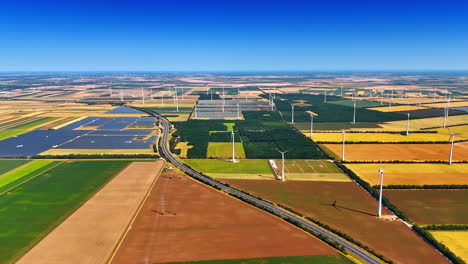 modern highway crosses the rural area. vast countryside with electricity power lines, solar panels and wind mills on sunny day. aerial view