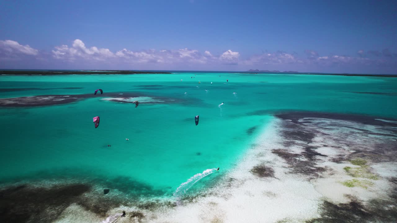 Kite surfers gliding over turquoise waters in los roques under a clear blue sky , aerial view