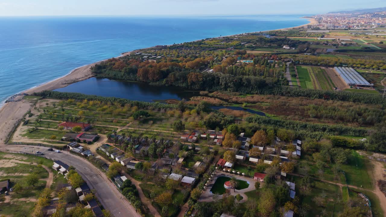 Drone view flying over the tordera river mouth meeting the mediterranean sea, showing a coastal campsite, agricultural fields, and the sandy beach on a sunny day in catalonia, spain