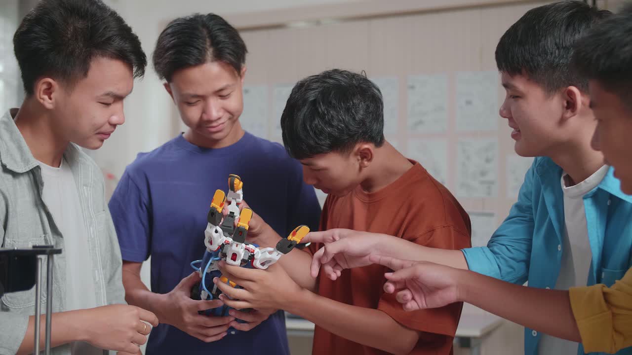 un grupo de jóvenes asiáticos con una computadora portátil e impresión 3d celebrando el éxito en el ensamblaje de una mano cyborg mientras trabajan en casa