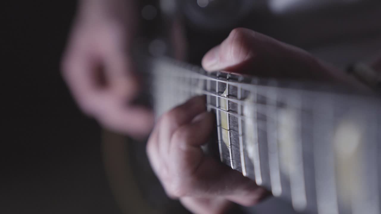 Looking down neck of electric guitar while man plays. Focus on frets, fingers