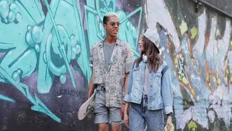 hipster couple in stylish clothes in love talking and walking down the street near a graffity wall