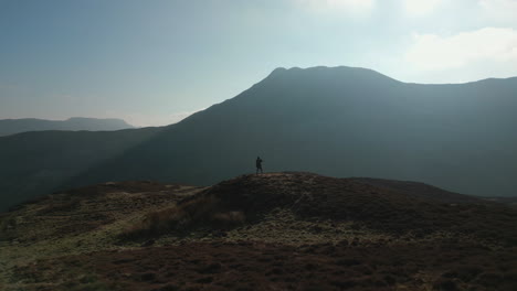 Hiker-walking-to-hilltop-with-misty-shadow-mountain-in-background-in-English-Lake-District-UK