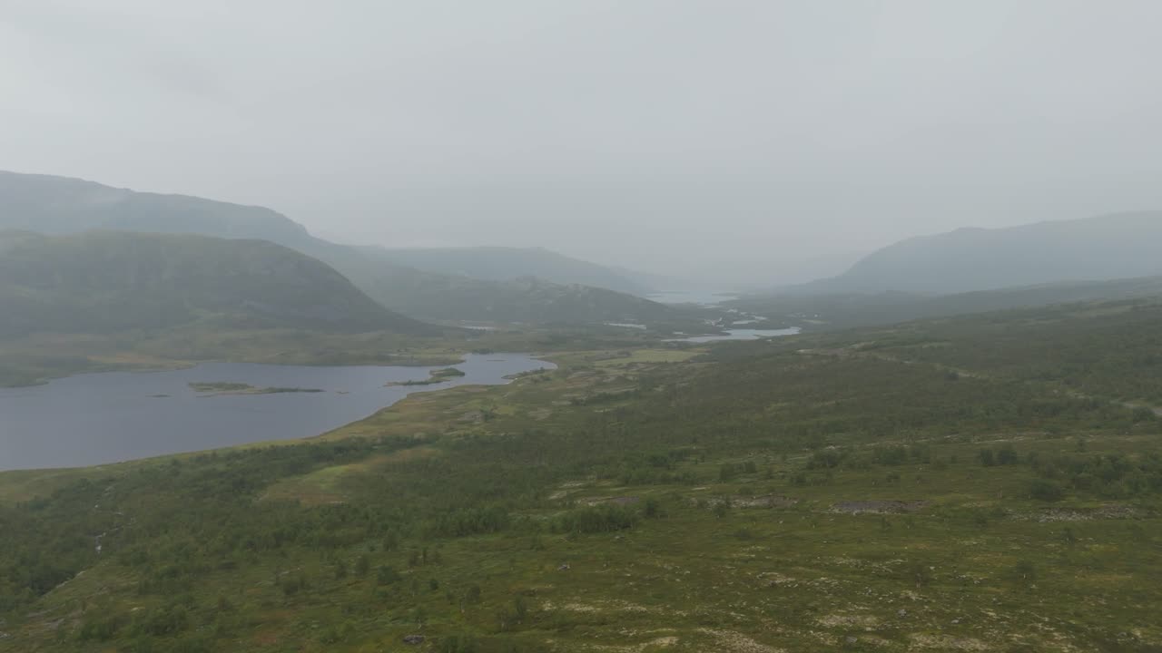 Aerial view of a foggy landscape featuring a tranquil lake surrounded by lush hillside and wilderness. Ideal for nature and serenity concepts.