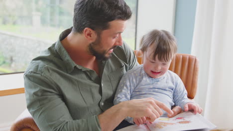 Padre-Con-Hija-Con-Síndrome-De-Down-Leyendo-Un-Libro-Juntos-En-Casa