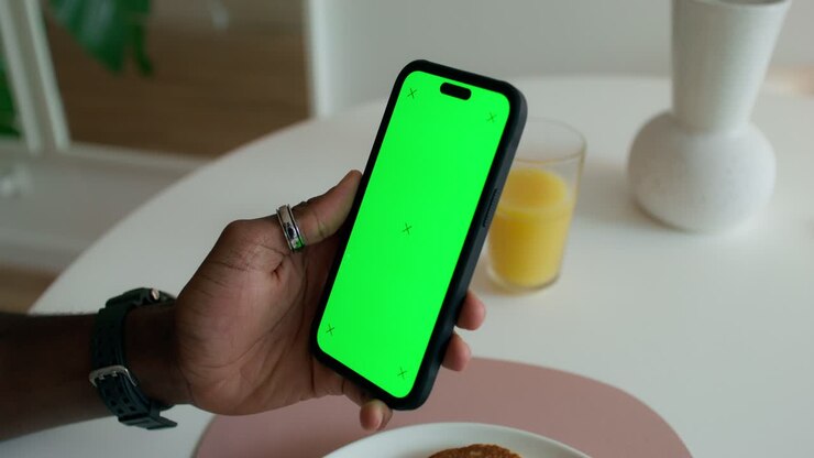Person holding a smartphone with a green screen at a breakfast table