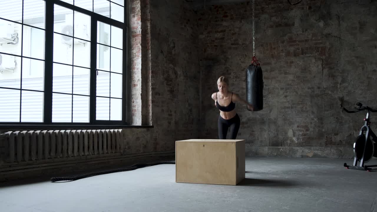 건강하고 운동적인 여성은 버려진 공장 체육관에서 박스 점프를 합니다.