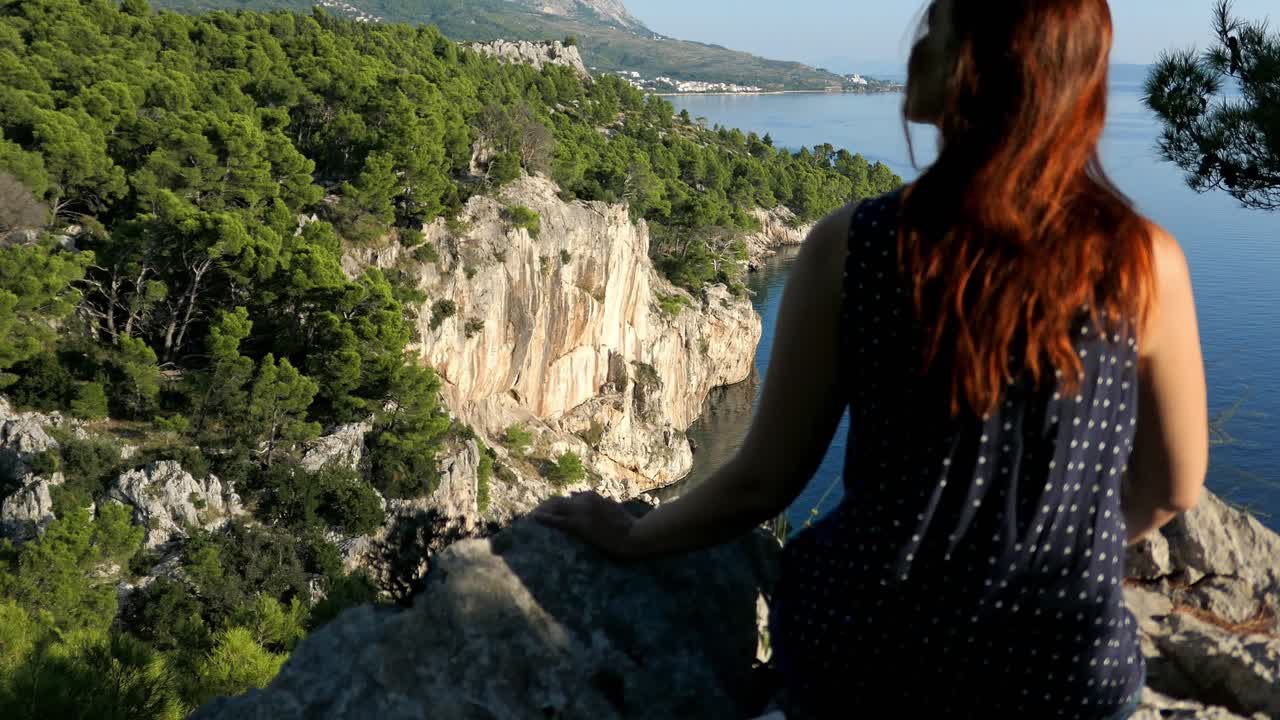 mujer sentada en el borde de un acantilado de montaña mirando la impresionante vista del mar