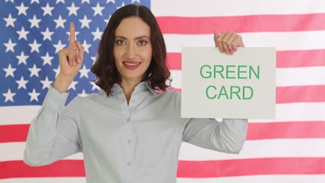 woman holding a "green card" sign in front of an american flag