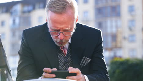 old people and smartphone concept. close up of senior man playing videogames on street