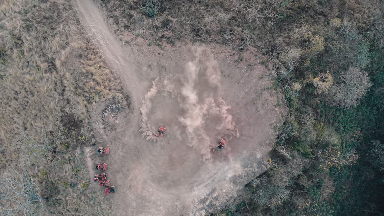 Drone view of ATVs creating circular dust trails in an open clearing surrounded by forest.