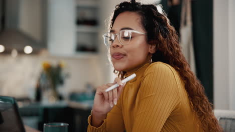 a woman with curly hair and glasses is thinking while working at home