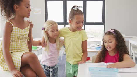 Video-of-happy-diverse-girls-sitting-at-school-desk,-talking-and-laughing