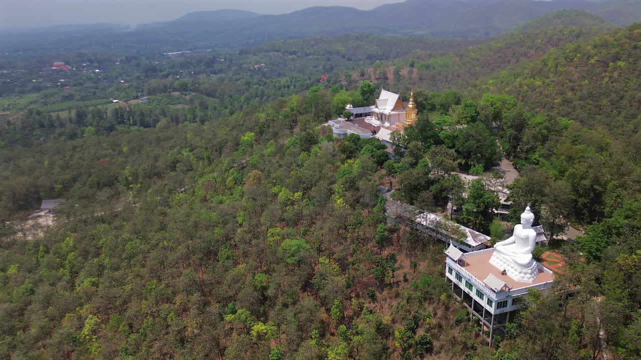 Hilltop Buddhist temple overlooks Chiang Mai valley with trees and misty air, aerial pan