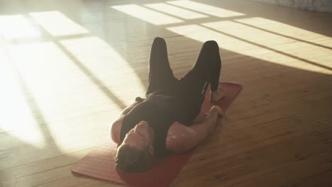 Top-view-of-a-man-who-pumps-his-pelvic-muscles-during-fitness.-Going-in-for-sports-a-man-in-a-black-sports-summer-uniform-lies