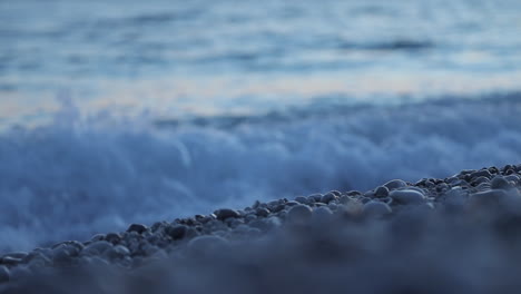 Ruhiger-Kiesstrand,-Nass-Von-Meereswellen,-Die-Auf-Verschwommenem-Hintergrund-Schäumen-Und-Spritzen