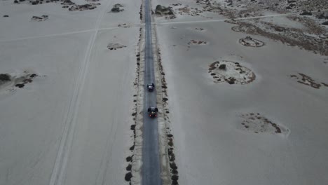 aerial drone tilt up shot over cars passing by on the road surrounded by mud volcanic soil in balochistan during evening time