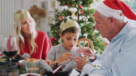 Sohn-Spielt-Mit-Weihnachtscracker-Neuheitsgeschenk-Und-Sitzt-Mit-Mutter-Und-Großvater-Am-Esstisch