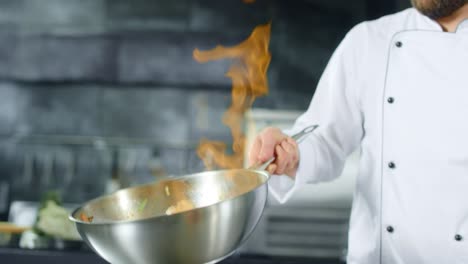 Chef-Cocinando-Comida-Con-Llama-De-Fuego-En-Una-Sartén-En-La-Cocina.-Manos-Del-Chef-Preparando-La-Comida