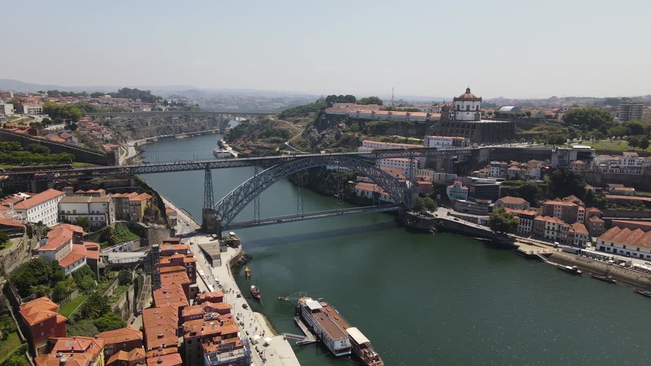 Drone captures Dom Luis I Bridge crossing Douro River between Porto and Vila Nova de Gaia. Surrounded by red rooftops, boats, and historic buildings, this iron structure stands as iconic city symbol