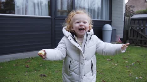 running toddler with winter jacket with big smile through the garden