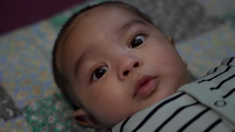 Close-Up-View-Of-Adorable-4-Month-Old-Indian-Baby-Boy-Looking-Wide-Eyed-At-Camera-Laying-On-Blanket-On-The-Floor