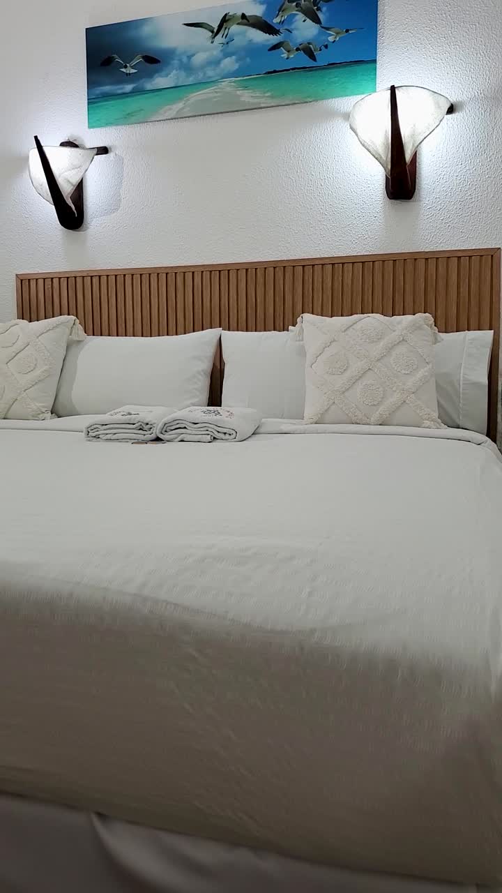 Spacious white bedroom interior with wooden bed with bedding and pillows. Vertical shot