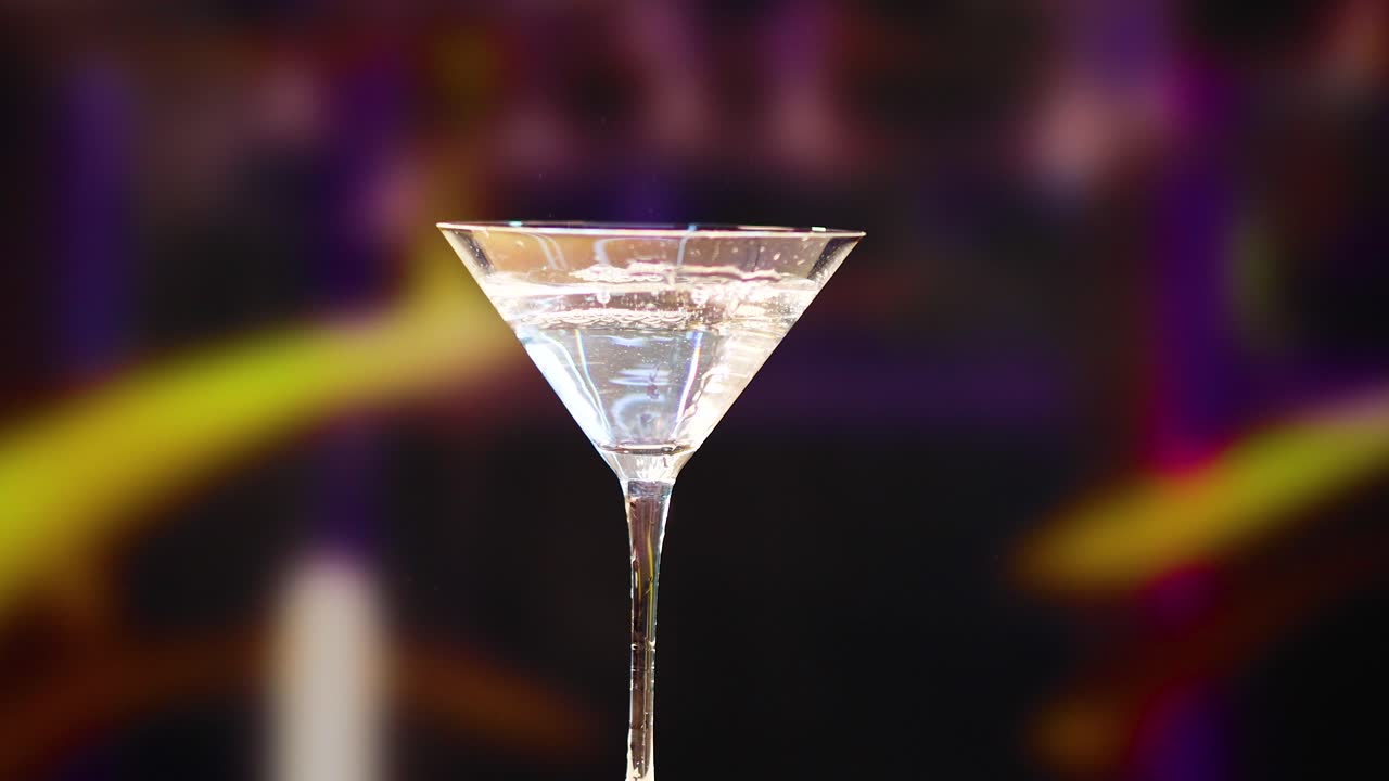 A martini is prepared with a citrus garnish in a dimly lit bar, highlighting the drink's elegance and sophistication