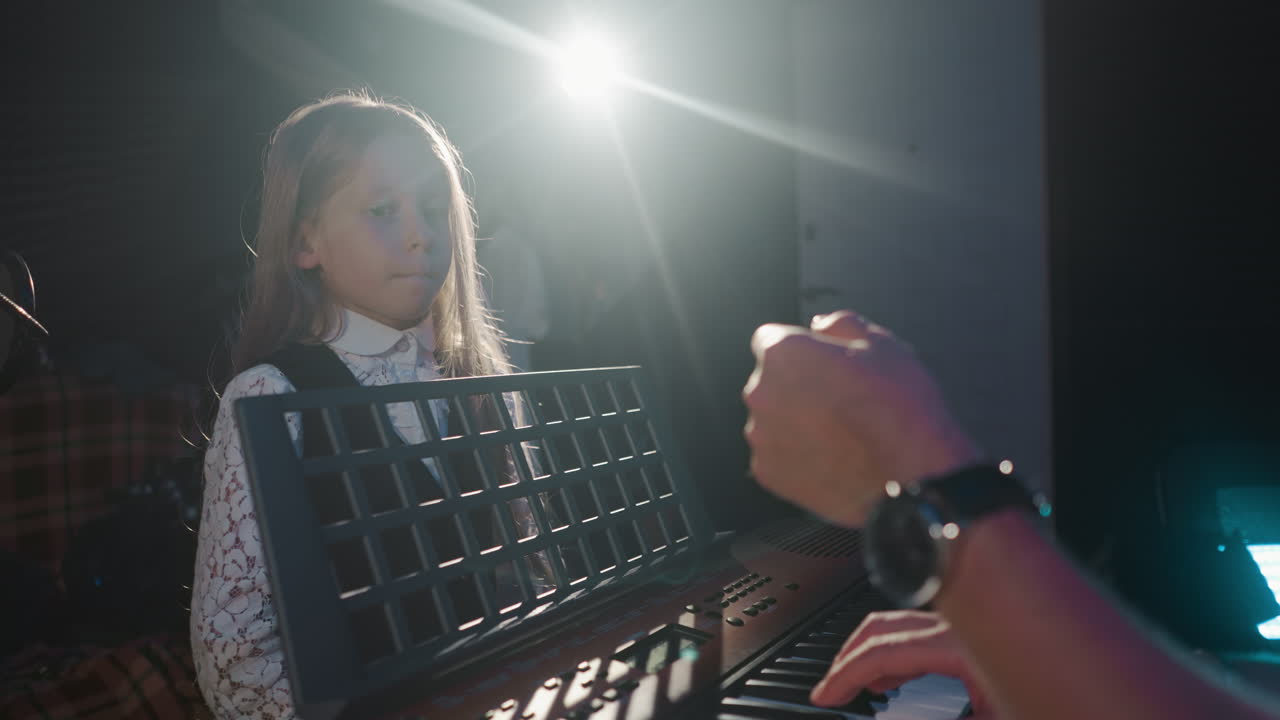 소녀는 스튜디오에서 노래하는 기술을 습득합니다. 작은 학생은 교실에서 신디사이저를 작동하는 음악가와 함께 보컬 기술을 연습합니다. 창의적인 아이.