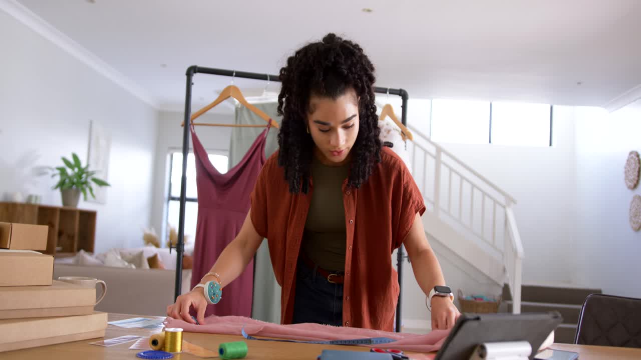 Femme adulte vérifiant une tablette, mesurant un tissu rose avec un mètre ruban, marquant et coupant pour un vêtement
