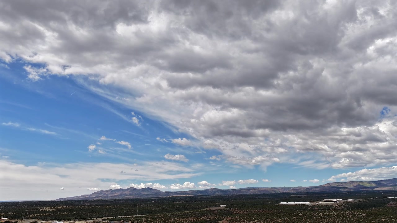 Un timelapse 4K con drone cattura strati di nuvole spettacolari che si muovono sopra mesas desertiche e montagne. Il movimento atmosferico cinematografico rivela un aspro paesaggio del sud-ovest e una geografia arida ad alta quota