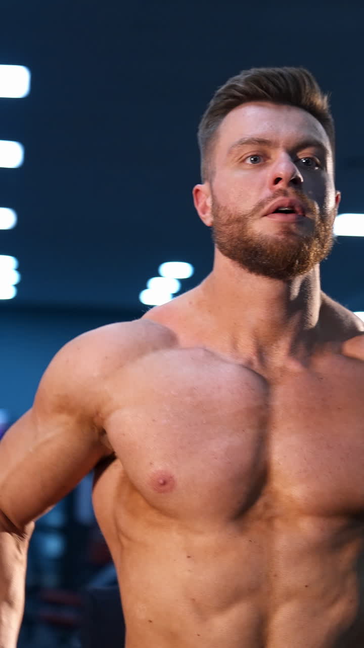 Athletic man in gym is posing to the camera. Bodybuilder with perfect body. Naked torso with perfect abs. Vertical video