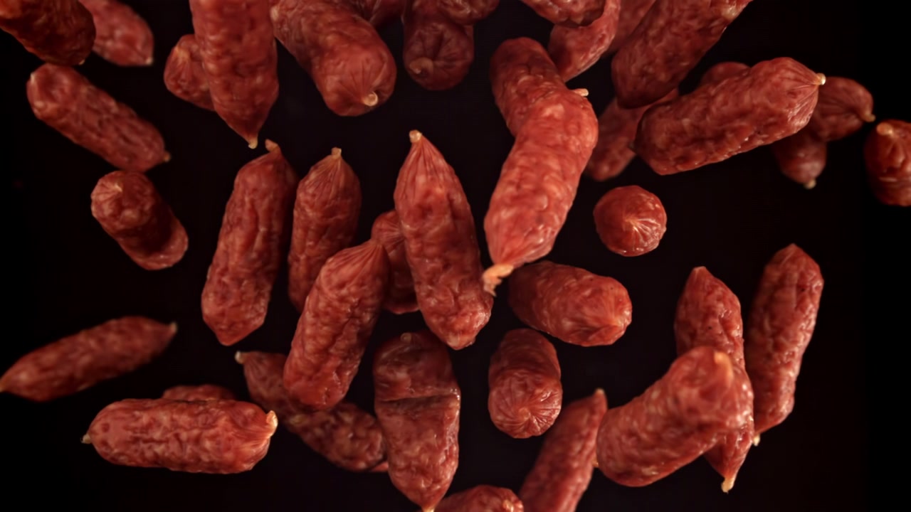 Mini kiełbaski salami spadające w zwolnionym tempie na czarnym tle