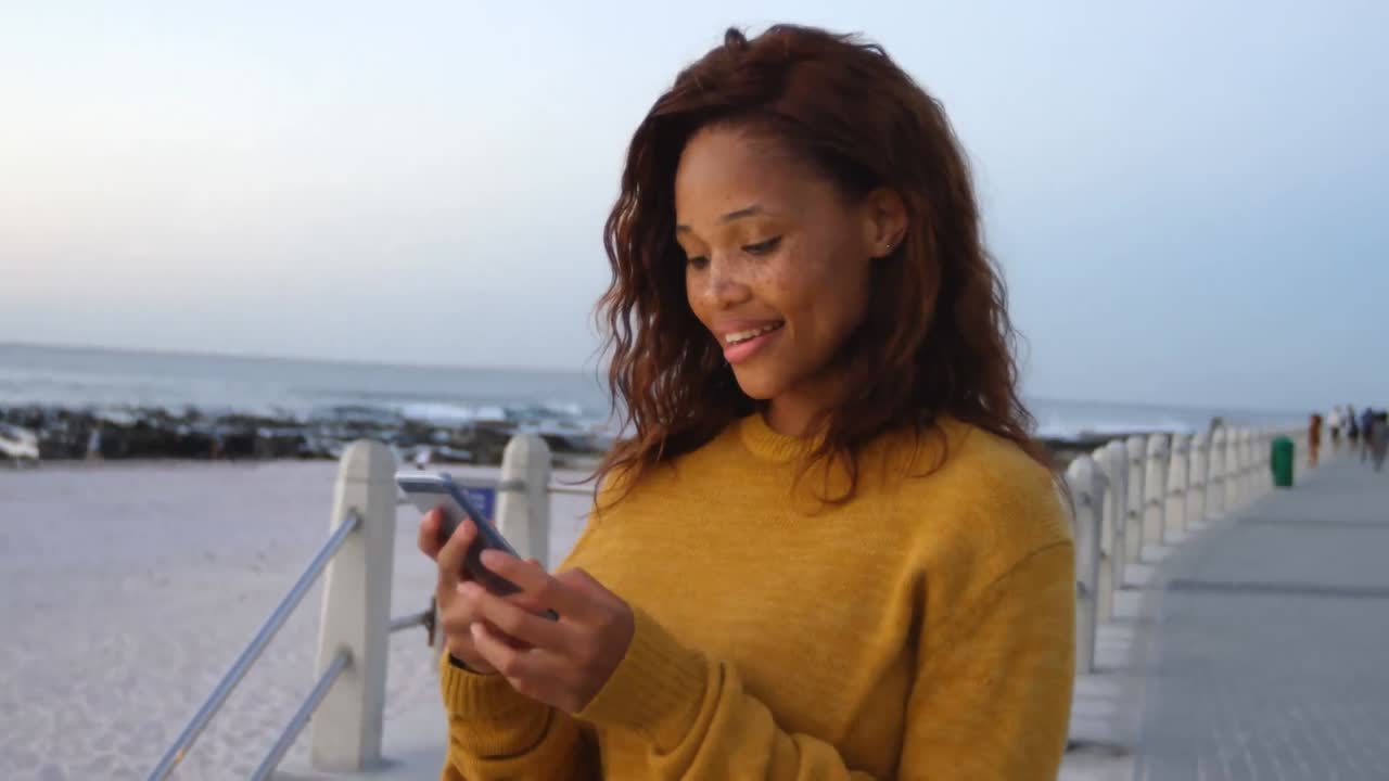 Smiling african american woman using smartphone at beach