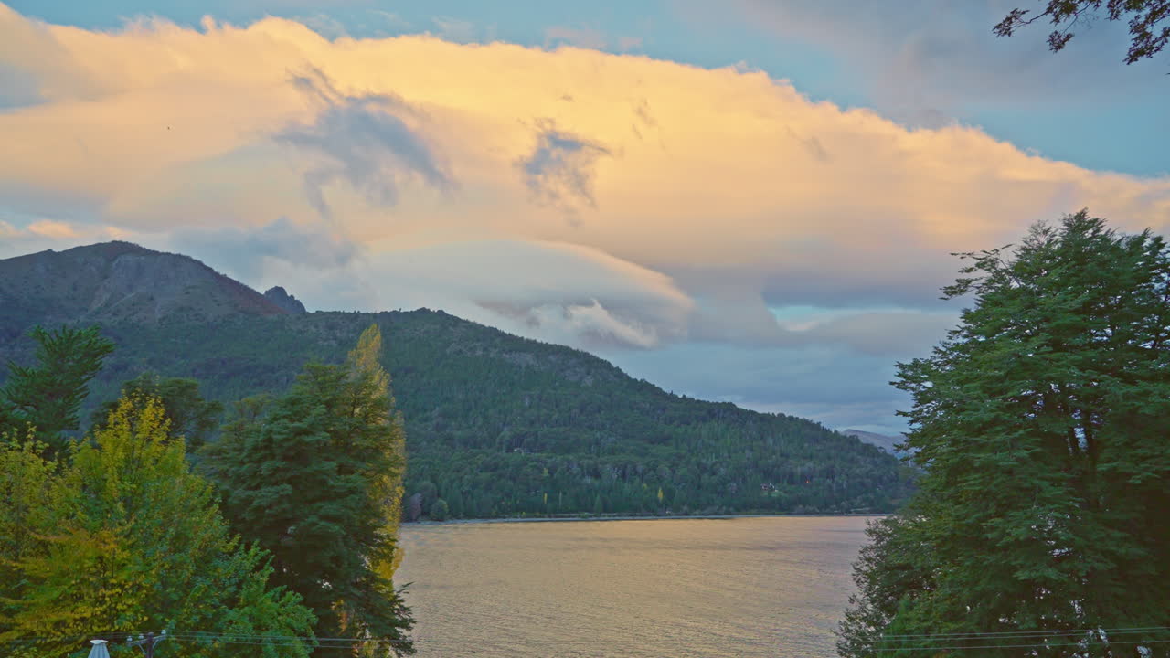 Naturskön sjö med skogklädda berg och gyllene moln vid solnedgången