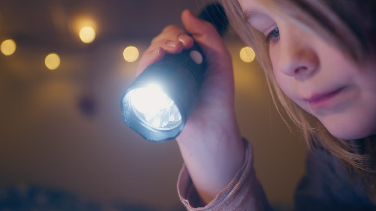 Atmósfera onírica mientras un niño pequeño usa una linterna para leer un libro por la noche