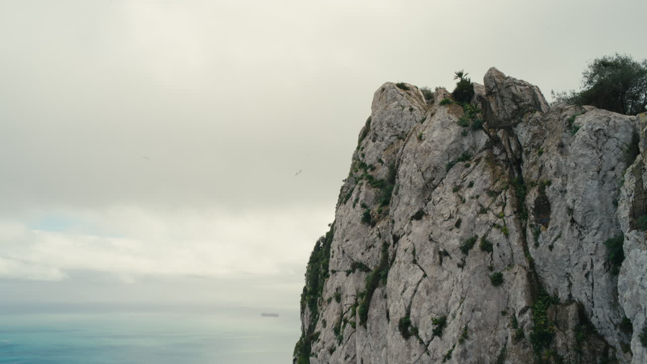 Vista spettacolare della celebre Rocca di Gibilterra che sovrasta il Mar Mediterraneo sotto cieli nuvolosi, con navi lontane all'orizzonte.