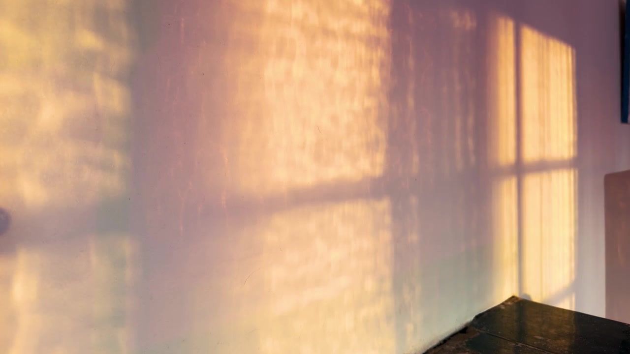 Timelapse of golden hour sunlight caustics and window shadow moving on wall