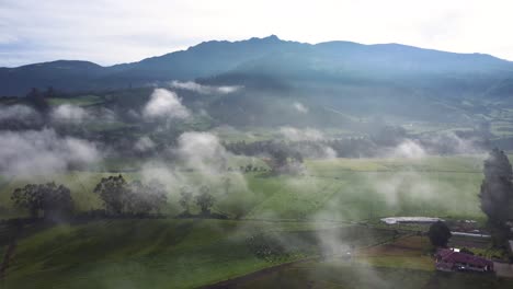 slow moving backwards aerial drone clip over fields and the clouds with the volcano pasochoa at the background in neblina, equador