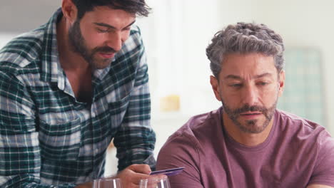 same sex male couple with credit card using laptop at home to book holiday or shop