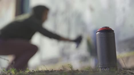 초점이 맞지 않는 남자가 배경의 벽에 낙서를 하고, 전경에 서서 스프레이 병에