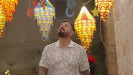 bearded caucasian tourist smiles at colorful alley lanterns, nazareth