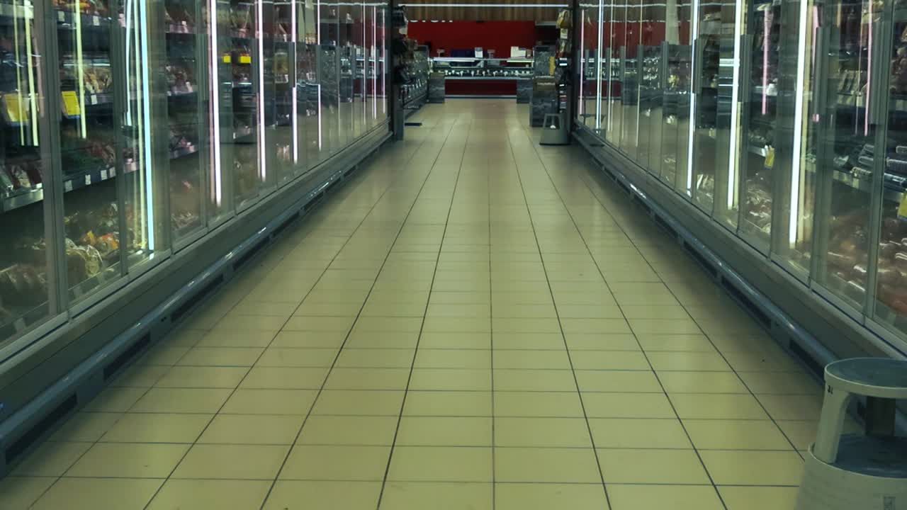 빈 식료품 가게 또는 슈퍼마켓 통로의 영상, 에 유리 문과 상품이있는 차가운 냉장고 캐비이 있습니다. 가게는 바닥에 돌 타일이 있습니다.