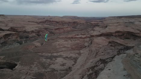 paraglider with colorful chute flying over canyons in utah, usa