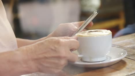 Mujer-Mayor-Tomando-Café-Mientras-Usa-El-Teléfono-Móvil-En-La-Cafetería-4k