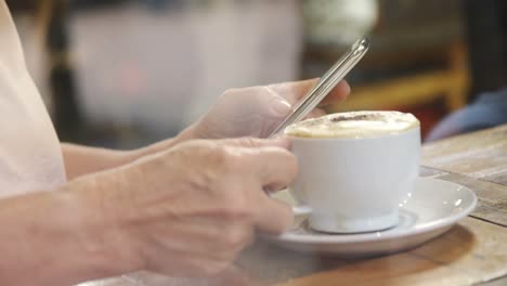 mujer mayor tomando café mientras usa teléfono móvil en el café 4k