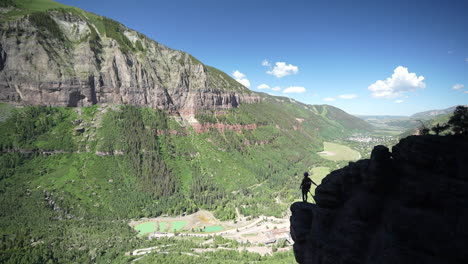 silhouette of climber standing on rock above abyss and amazing green valley landscape