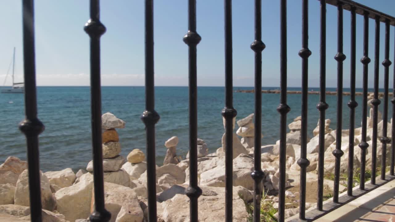 Vista serena sull'oceano attraverso una recinzione metallica con pietre impilate