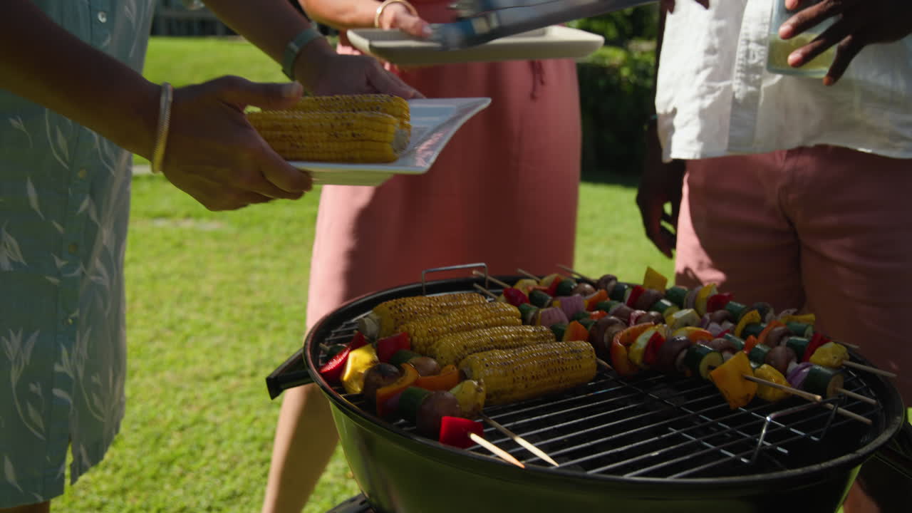 Grilling corn and vegetables in garden, diverse senior friends enjoying summer barbecue together
