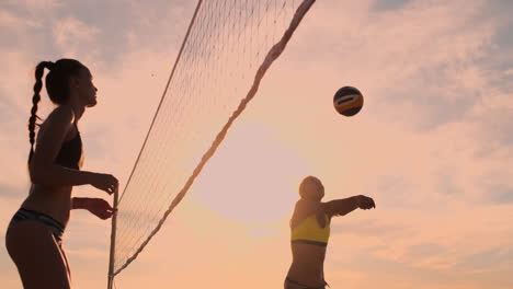 Las-Chicas-Del-Partido-De-Voleibol-De-Playa-Golpean-La-Pelota-En-Cámara-Lenta-Al-Atardecer-En-La-Arena.